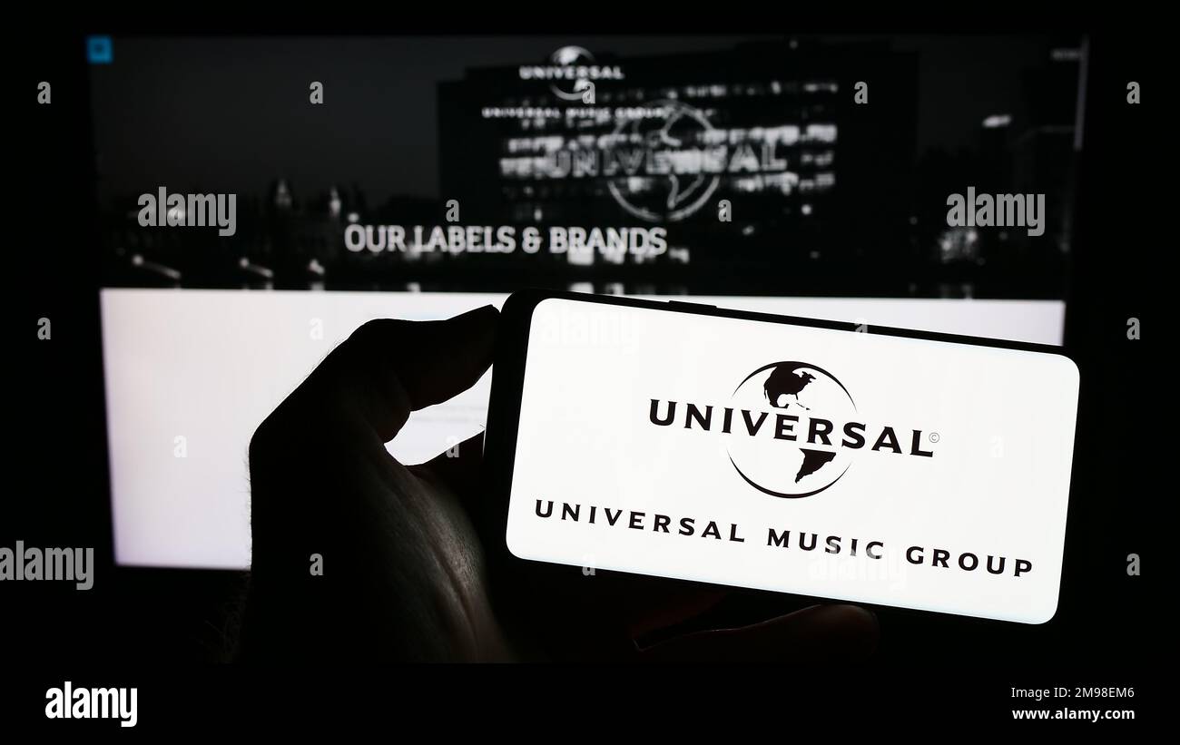 Persona che detiene il cellulare con il logo della società Universal Music Group N.V. (UMG) sullo schermo di fronte alla pagina Web aziendale. Messa a fuoco sul display del telefono. Foto Stock