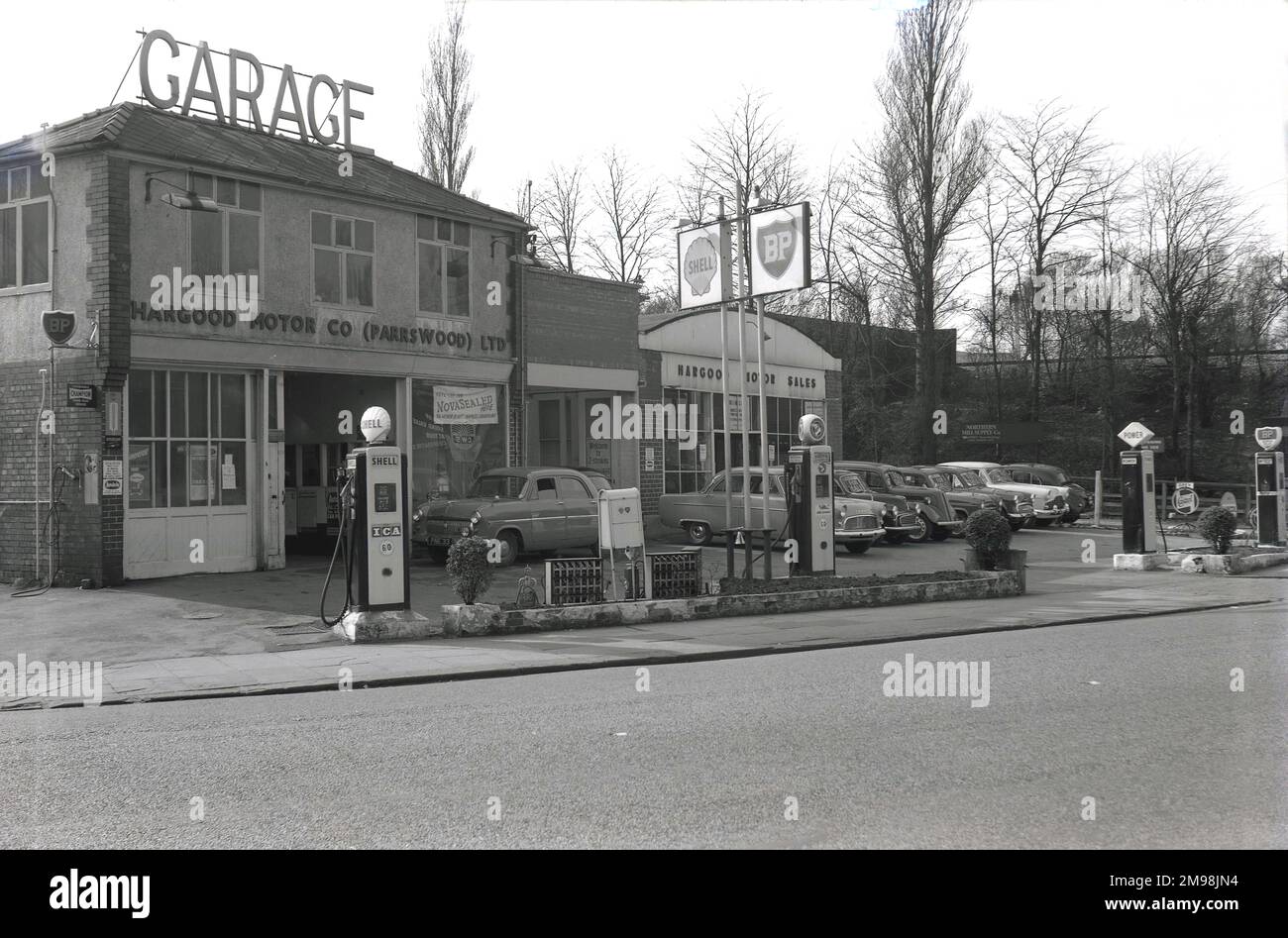 1957, storico, esterno dell'Harbood Motor Co sulla Wilmslow Rd, Didsbury, Manchester, Inghilterra, Regno Unito. La parola Garage è esposta in grandi lettere maiuscole sul tetto dell'edificio a due piani e le auto del giorno sono parcheggiate all'esterno del reparto vendite motori a destra dell'immagine. Come si può vedere dai cartelli e dalle pompe di benzina sul piazzale, diversi marchi di carburante tra cui BP, Shell, Power e National, sono stati offerti all'automobilista di quest'epoca. Foto Stock