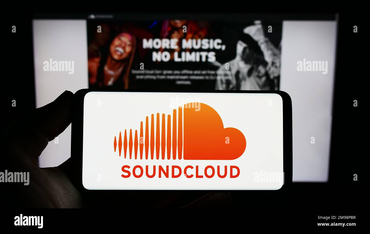 Persona che tiene in mano uno smartphone con il logo della società tedesca di condivisione musicale SoundCloud sullo schermo di fronte al sito Web. Messa a fuoco sul display del telefono. Foto Stock