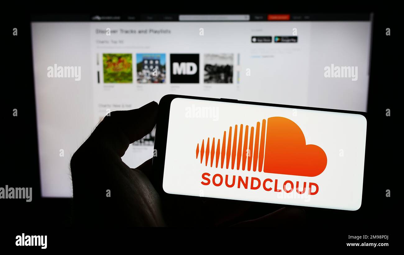 Persona che tiene il cellulare con il logo della società tedesca di condivisione di musica SoundCloud sullo schermo di fronte alla pagina Web aziendale. Messa a fuoco sul display del telefono. Foto Stock