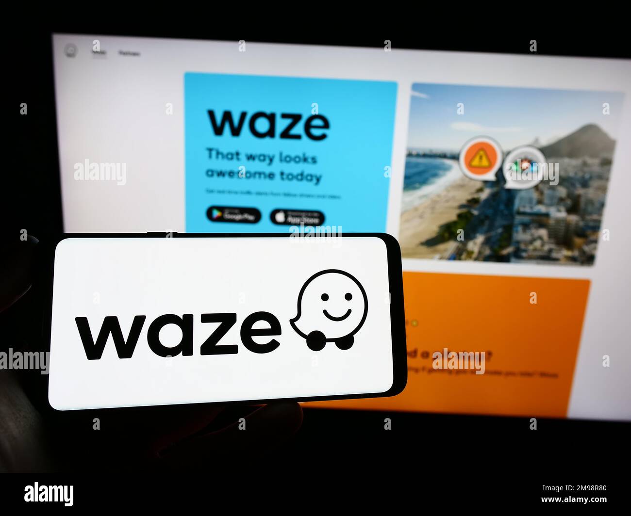 Persona che tiene uno smartphone con il logo della società di navigazione israeliana Waze Mobile Ltd. Sullo schermo di fronte al sito Web. Messa a fuoco sul display del telefono. Foto Stock