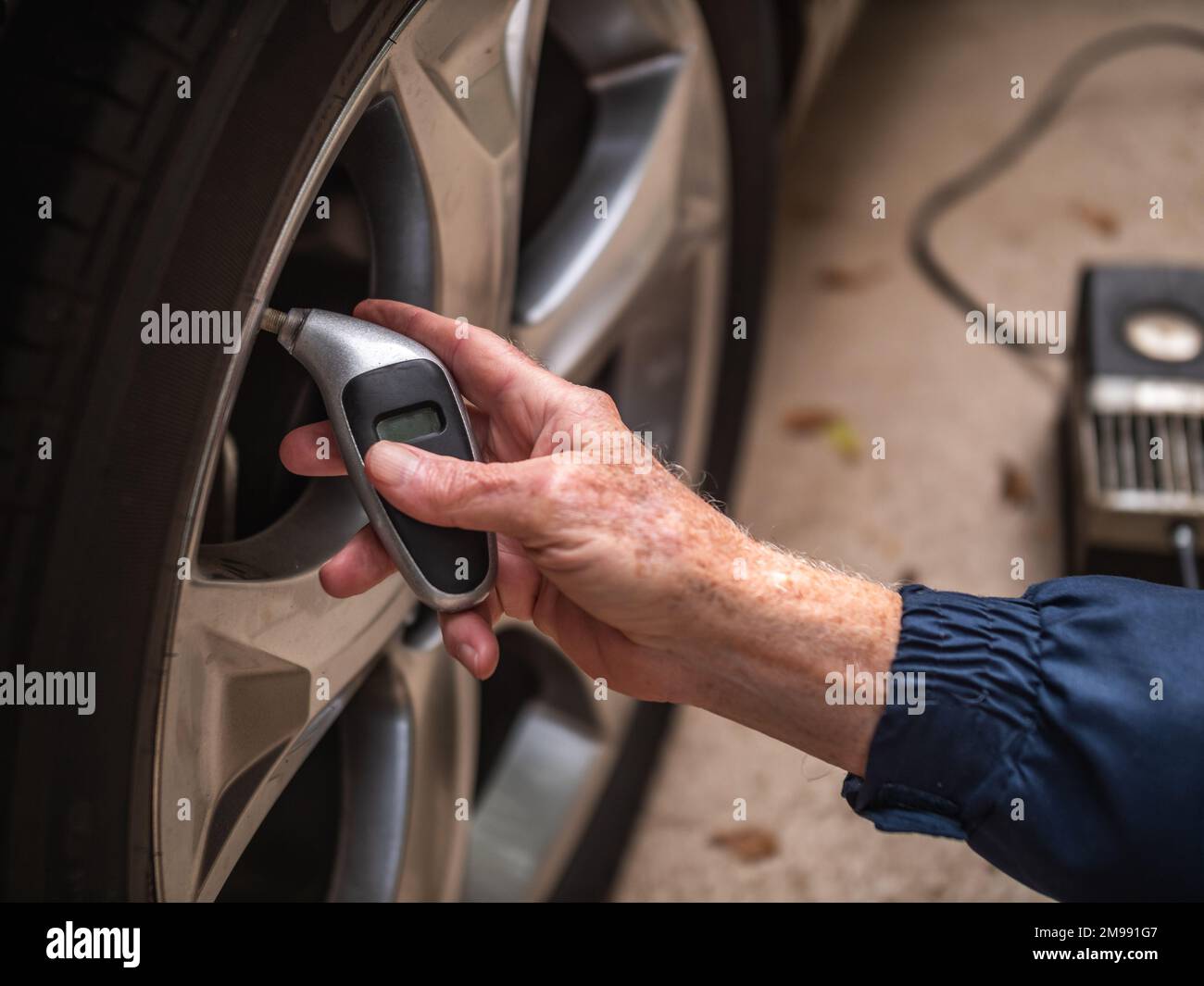Controllo meccanico degli pneumatici per auto per verificarne il corretto gonfiaggio. Uomo che utilizza un manometro digitale per controllare la pressione dell'aria degli pneumatici della vettura. Foto Stock
