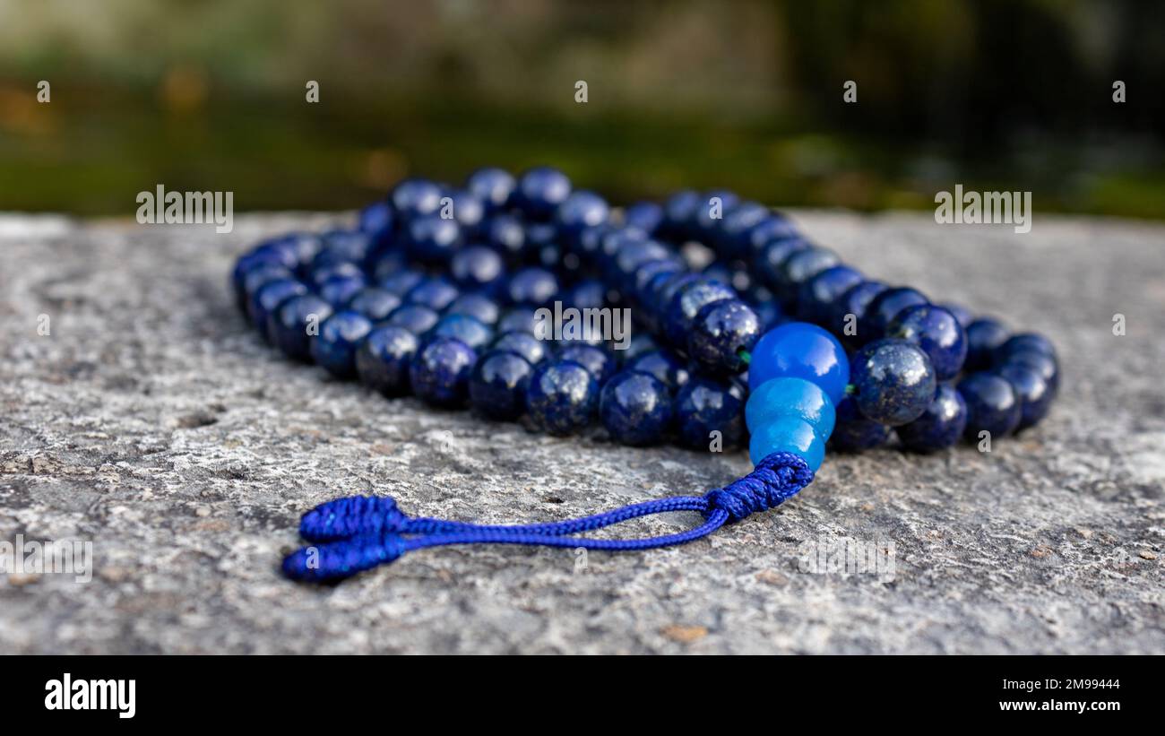 Perline di preghiera blu buddista mala (lapislazzuli) su pietra, primo piano. Consapevolezza e meditazione japa accessorio. Foto Stock