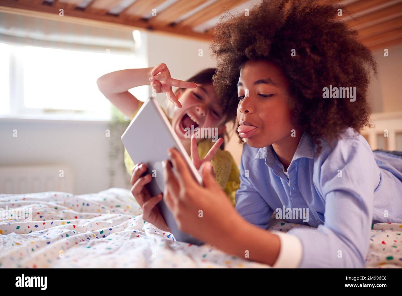 Ragazza e ragazzo in camera da letto sdraiati sul letto utilizzando il tablet digitale e tirando le facce divertente insieme Foto Stock