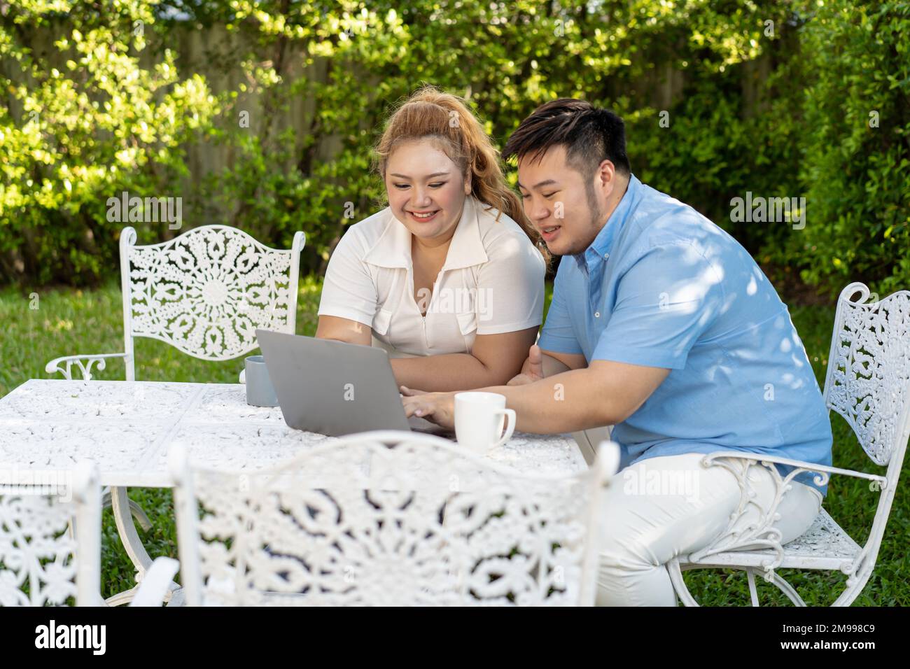 Giovane coppia asiatica chubby utilizzando un computer portatile nel parco verde all'aperto insieme. Felice uomo sorridente e donna che lavorano a distanza e avviare il proprio business insieme Foto Stock