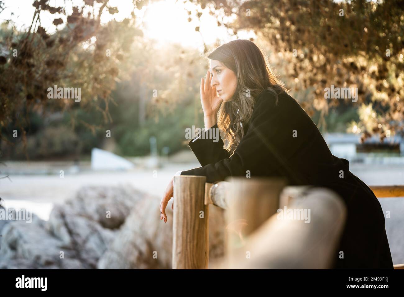 Donna triste vestita di nero guardando il mare con il tramonto sullo sfondo Foto Stock