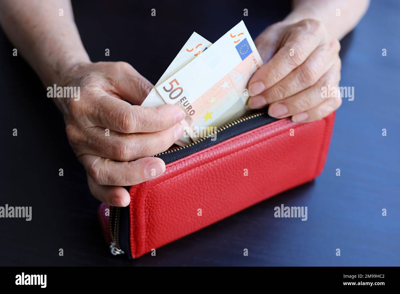 Banconote in euro in portafoglio rosso in mani stropicciate di donna anziana. Concetto di pagamenti e assistenza pensionistica, risparmio, pensionamento in Europa Foto Stock
