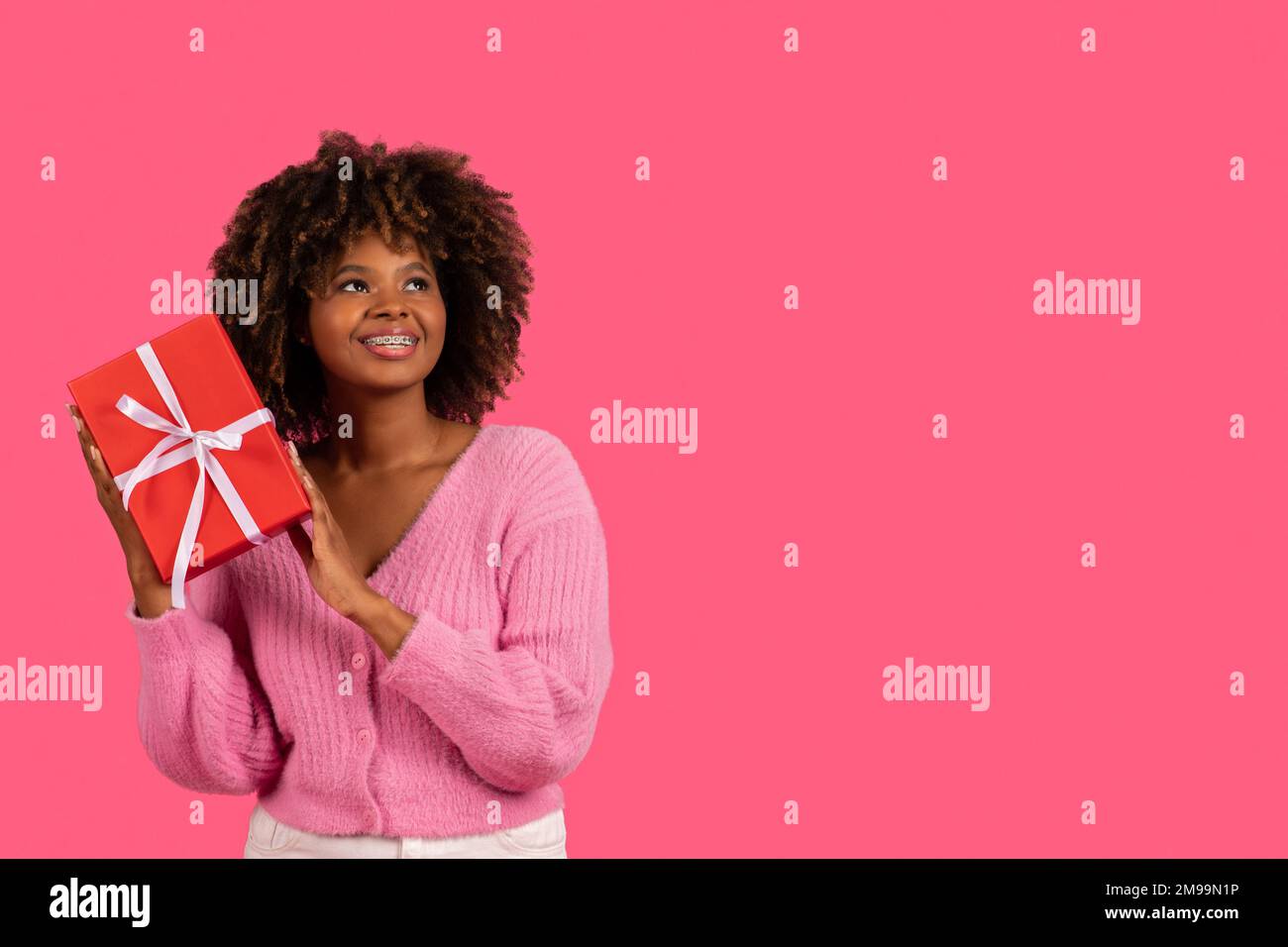 Giovane donna afroamericana sorridente con bretelle che tengono la scatola  del regalo e che guarda lo spazio vuoto Foto stock - Alamy