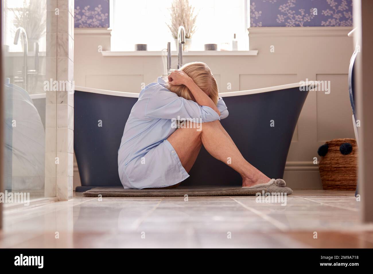 Menopausale Donna matura che soffre con incontinenza seduta sul pavimento del bagno a casa Foto Stock