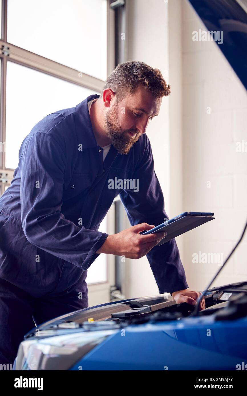 Meccanico maschile in officina che utilizza il software diagnostico sul tablet digitale per la manutenzione del motore dell'auto Foto Stock