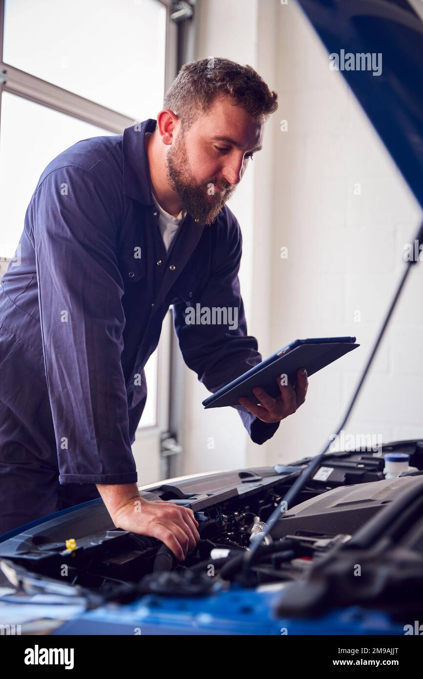 Meccanico maschile in officina che utilizza il software diagnostico sul tablet digitale per la manutenzione del motore dell'auto Foto Stock