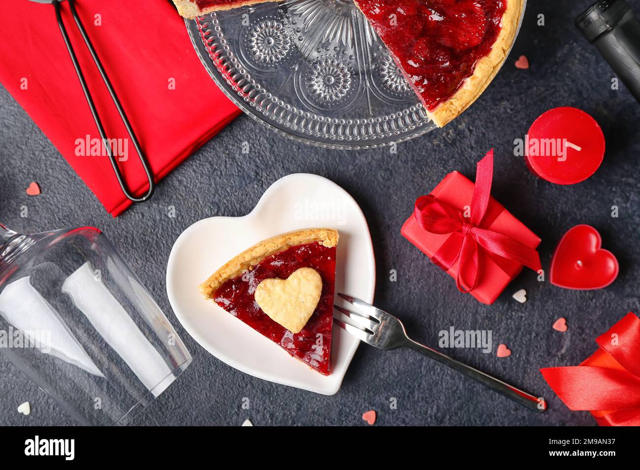 Piatto a forma di cuore con un pezzo di torta di fragole dolci, cuori di  biscotti, regali, vetro e candele romantiche per San Valentino su sfondo  scuro Foto stock - Alamy