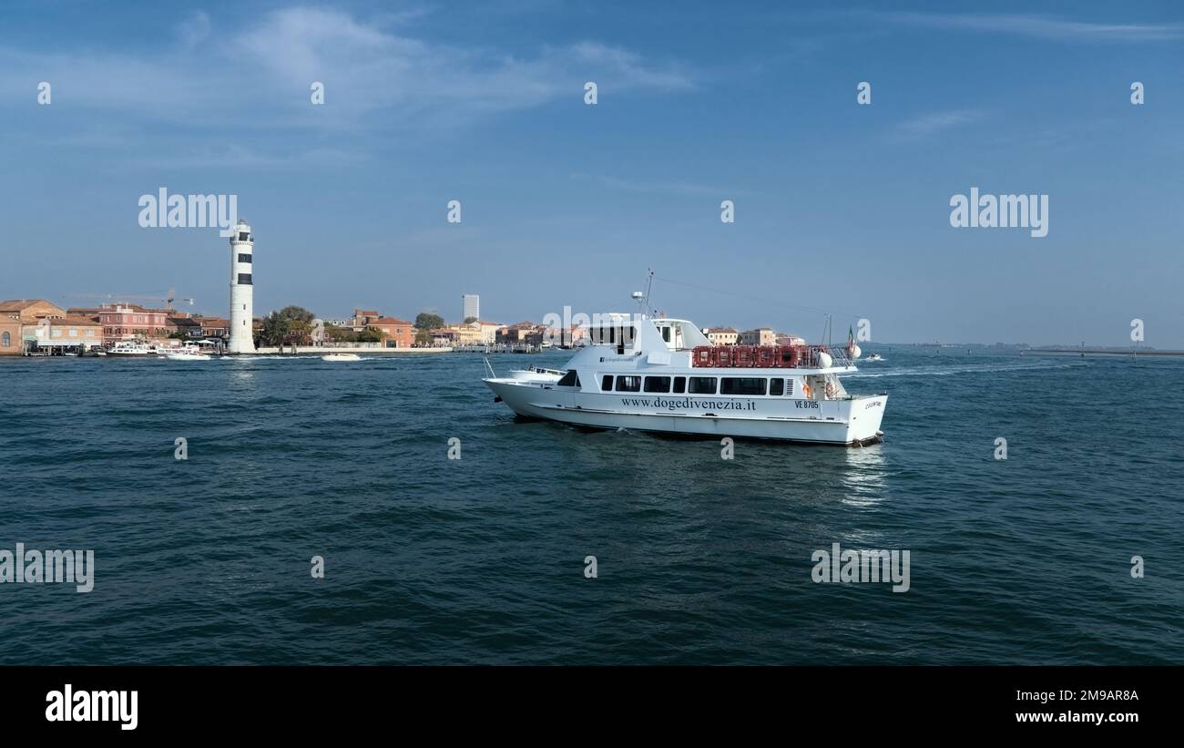 Un piccolo yacht bianco sta andando verso la riva con una torre del tempo. Foto Stock