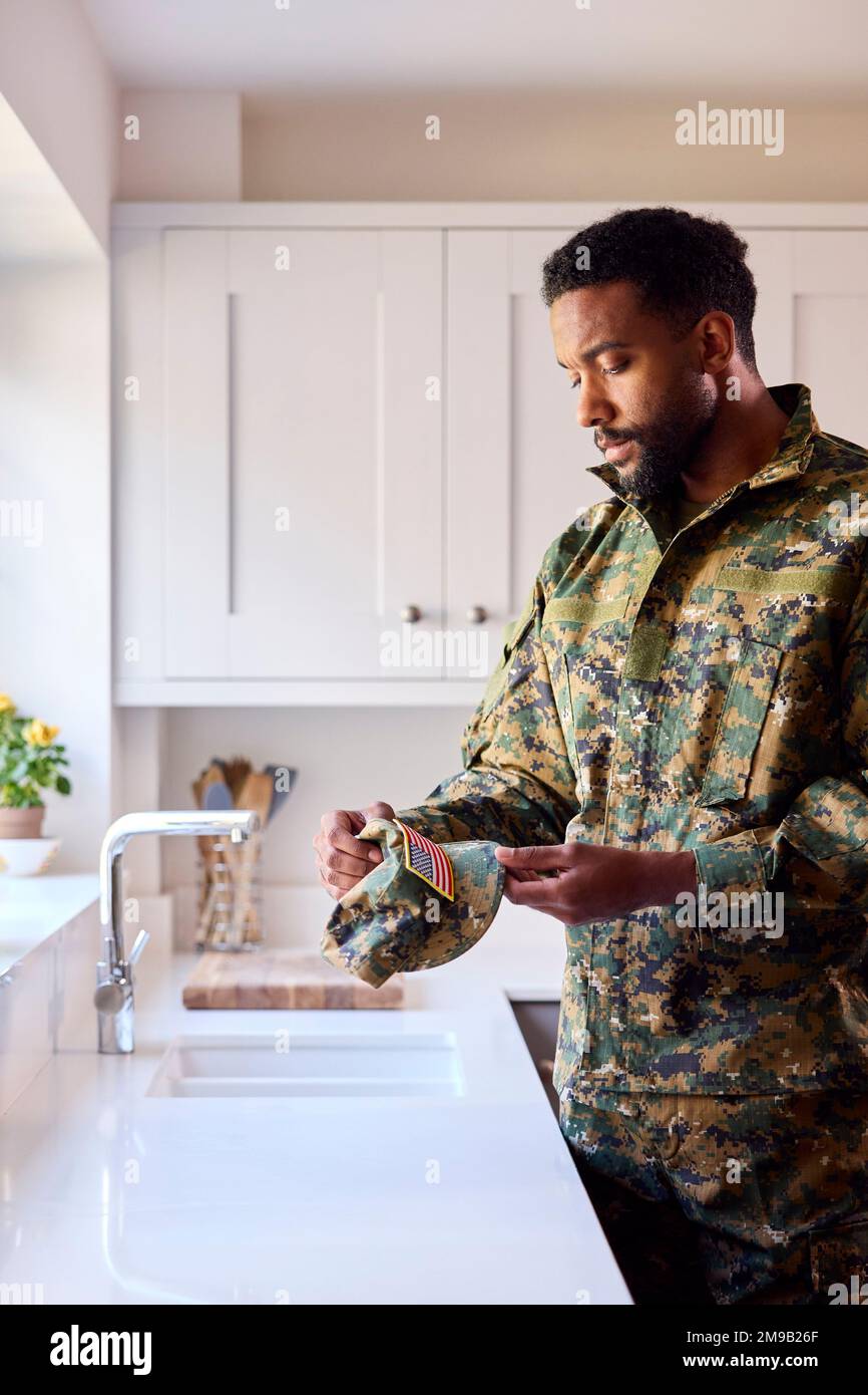 Soldato maschile premuroso americano in uniforme guardando Cap Badge in cucina in partenza casa Foto Stock