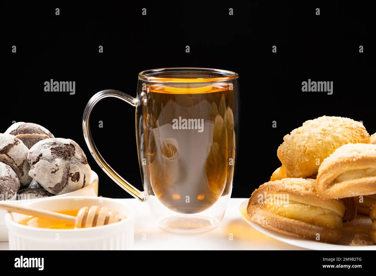 Tè al miele con biscotti al cacao e torte con farcitura cremosa su fondo nero. Foto Stock