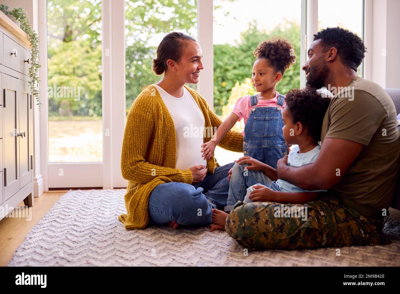 Famiglia militare con madre incinta seduta al piano nella sala a casa Foto Stock