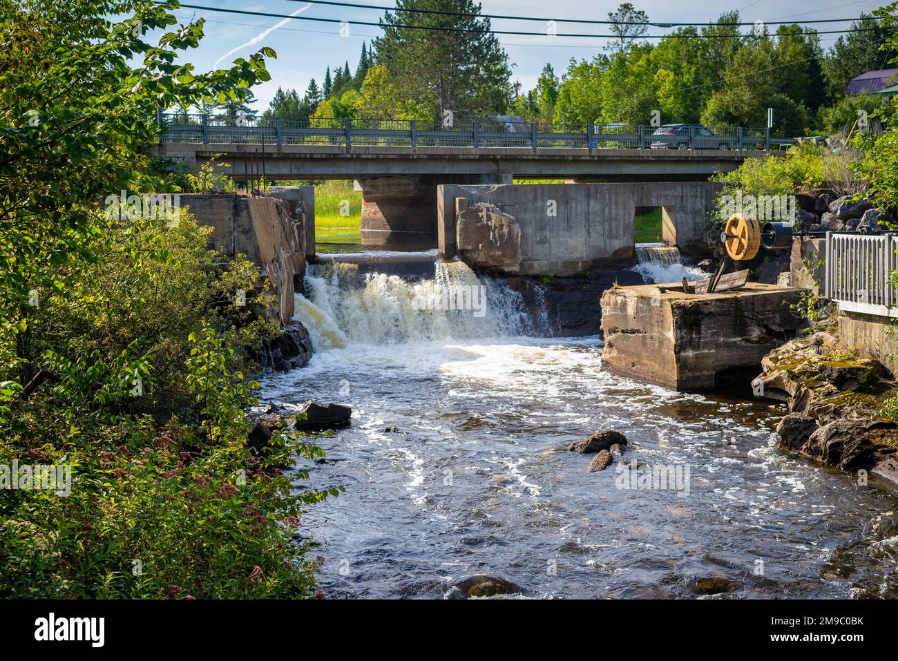 Un ponte stradale su un piccolo fiume e una diga rotta situato nel Laurentians, Quebec, Canada. Preso su un pomeriggio di estate di sole senza gente. Foto Stock