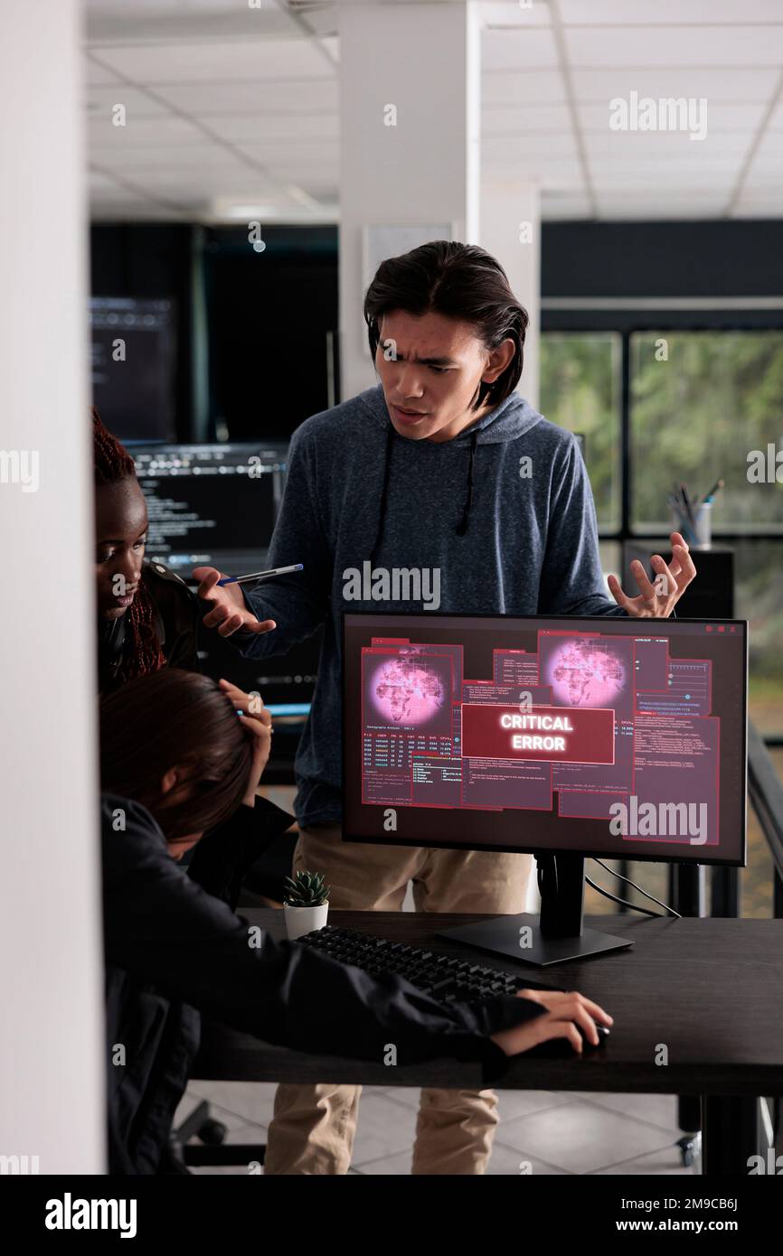 Team multietnico di programmatori IT che hanno violato l'avviso di violazione del server e della sicurezza sul display del pc, cercando di risolvere il problema dell'hacking. Si è verificato un messaggio di errore critico lampeggiante sullo schermo. Foto Stock