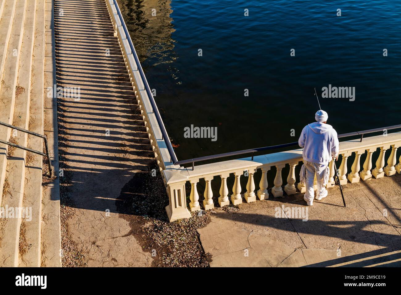 Uomo afro-americano che pesca lungo il sentiero di pietra illuminato dal sole; Fairmount Water Works; Schuylkill River; Philadelphia; Pennsylvania; STATI UNITI Foto Stock
