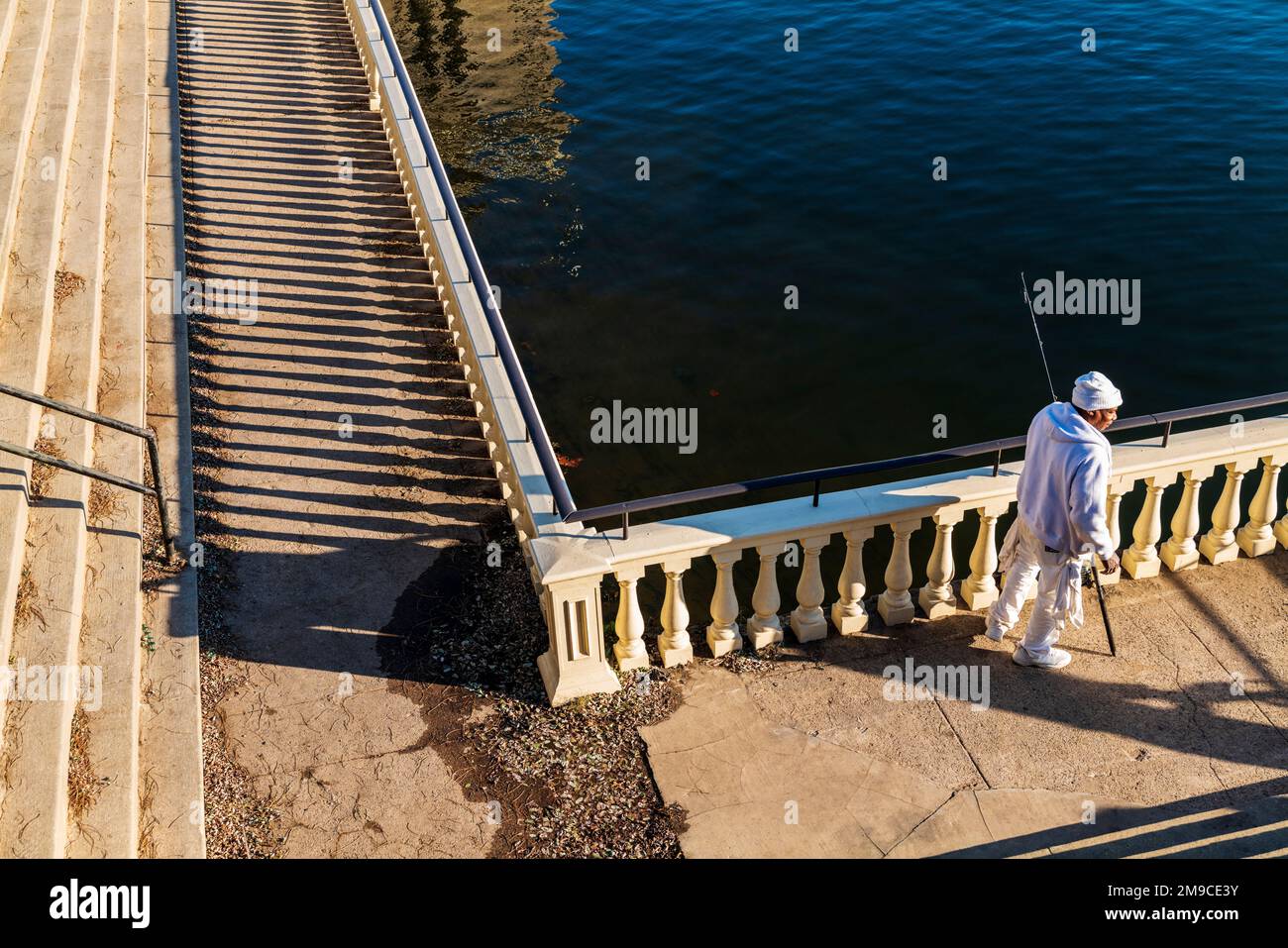 Uomo afro-americano che pesca lungo il sentiero di pietra illuminato dal sole; Fairmount Water Works; Schuylkill River; Philadelphia; Pennsylvania; STATI UNITI Foto Stock