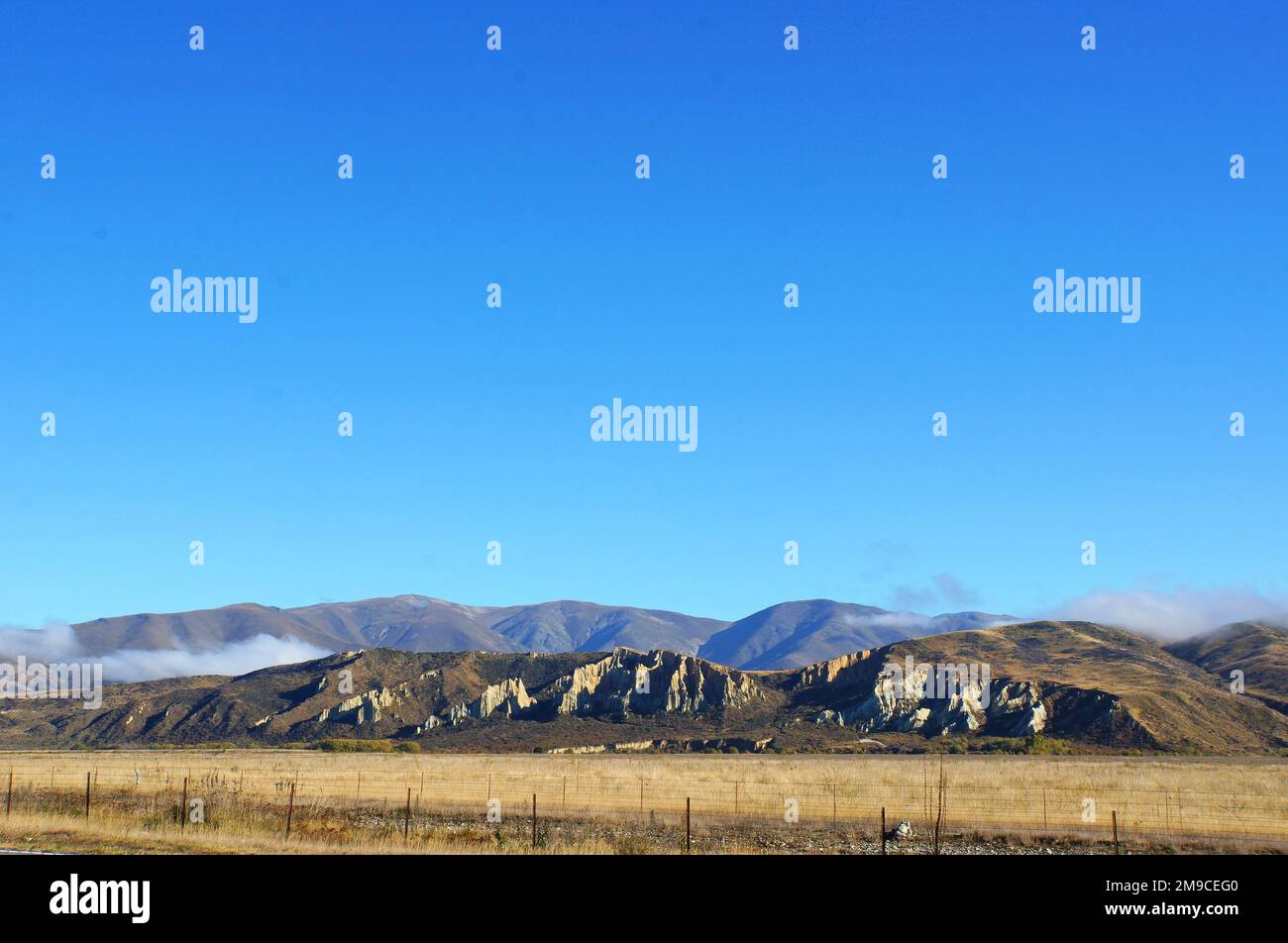 Panoramica Mackenzie District, South Canterbury, Nuova Zelanda ombreggiato blu catena montuosa e terreni agricoli secchi sotto il cielo blu brillante autunno. Foto Stock