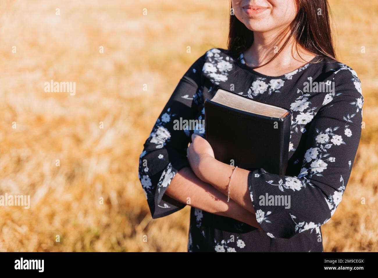 Ragazza cristiana irriconoscibile che tiene la sua bibbia sotto il suo braccio nel campo. Sola Scriptura. Spazio di copia Foto Stock