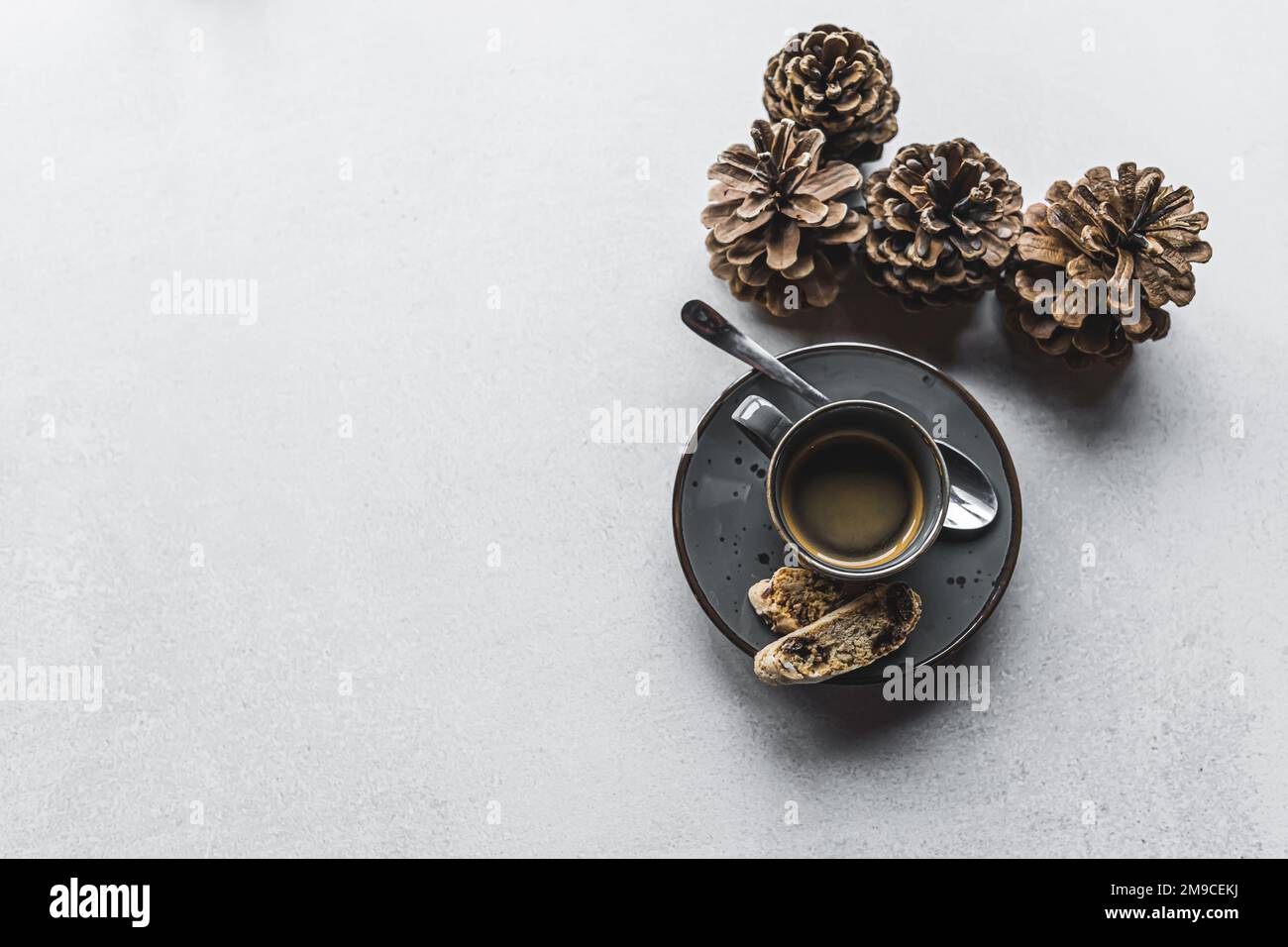 Shot top-down di tazza di caffè espresso su piattino con cucchiaio piccolo e due biscotti accanto a pineconi decorativi su tavolo di pietra. Autunno inverno vacanze drink. Scatto orizzontale. Foto di alta qualità Foto Stock