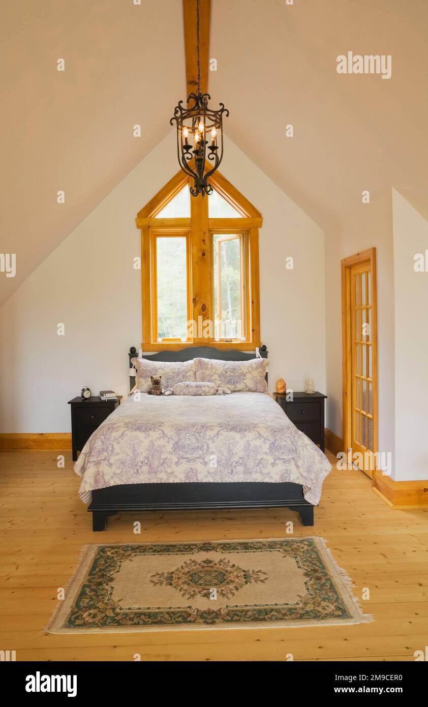 Letto queen size con testiera e poggiapiedi in legno color carbone nella camera da letto principale al piano superiore all'interno di una cabina in legno fresato. Foto Stock