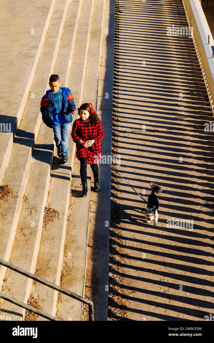 Giovane ragazzo e ragazza con cane da compagnia che saltano felicemente lungo il sentiero di pietra illuminato dal sole; Fairmount Water Works; Philadelphia; Pennsylvania; USA Foto Stock