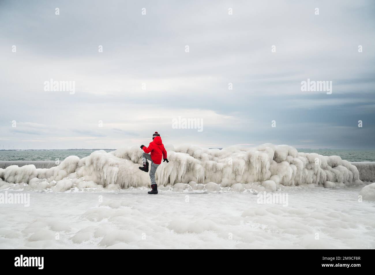 Bambino in cappotto rosso rompere il ghiaccio sul molo congelato il giorno d'inverno. Foto Stock