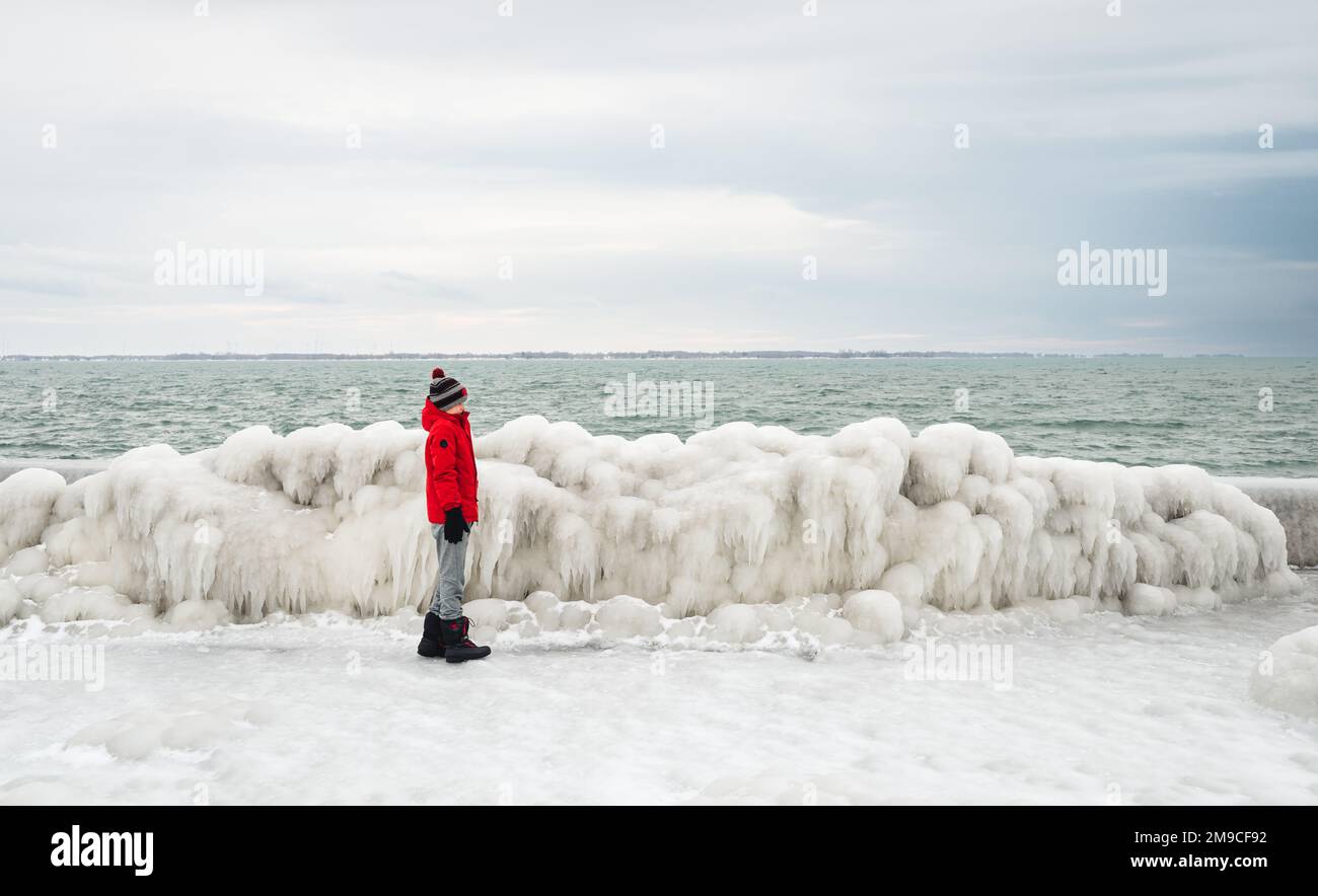 Bambino in cappotto rosso in piedi sul molo ghiacciato in inverno. Foto Stock