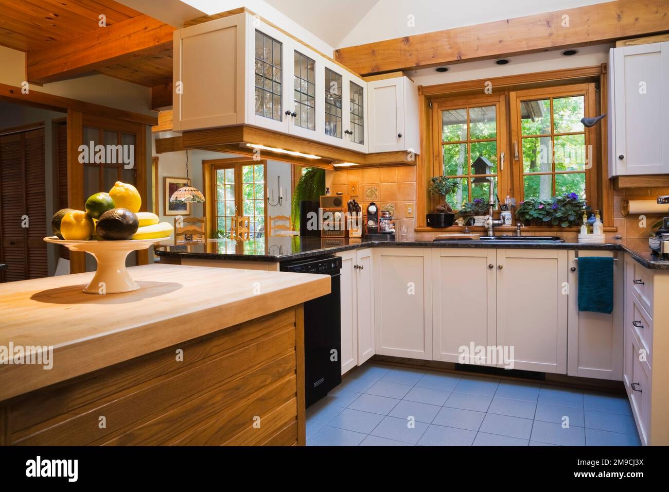 Cucina con isola in legno d'acero, armadi in legno bianco e ripiani in granito nero all'interno di una casa in legno di stile canadese. Foto Stock