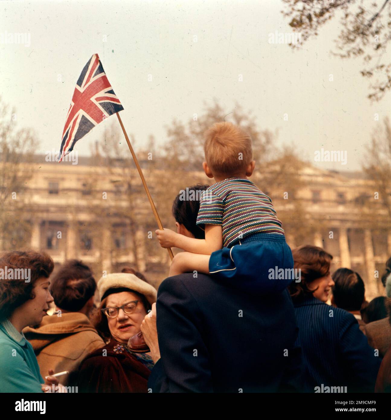 Un ragazzino si siede sulle spalle del padre e ondeggia la bandiera di Union Jack patriotticamente, forse alla regina Elisabetta II Foto Stock