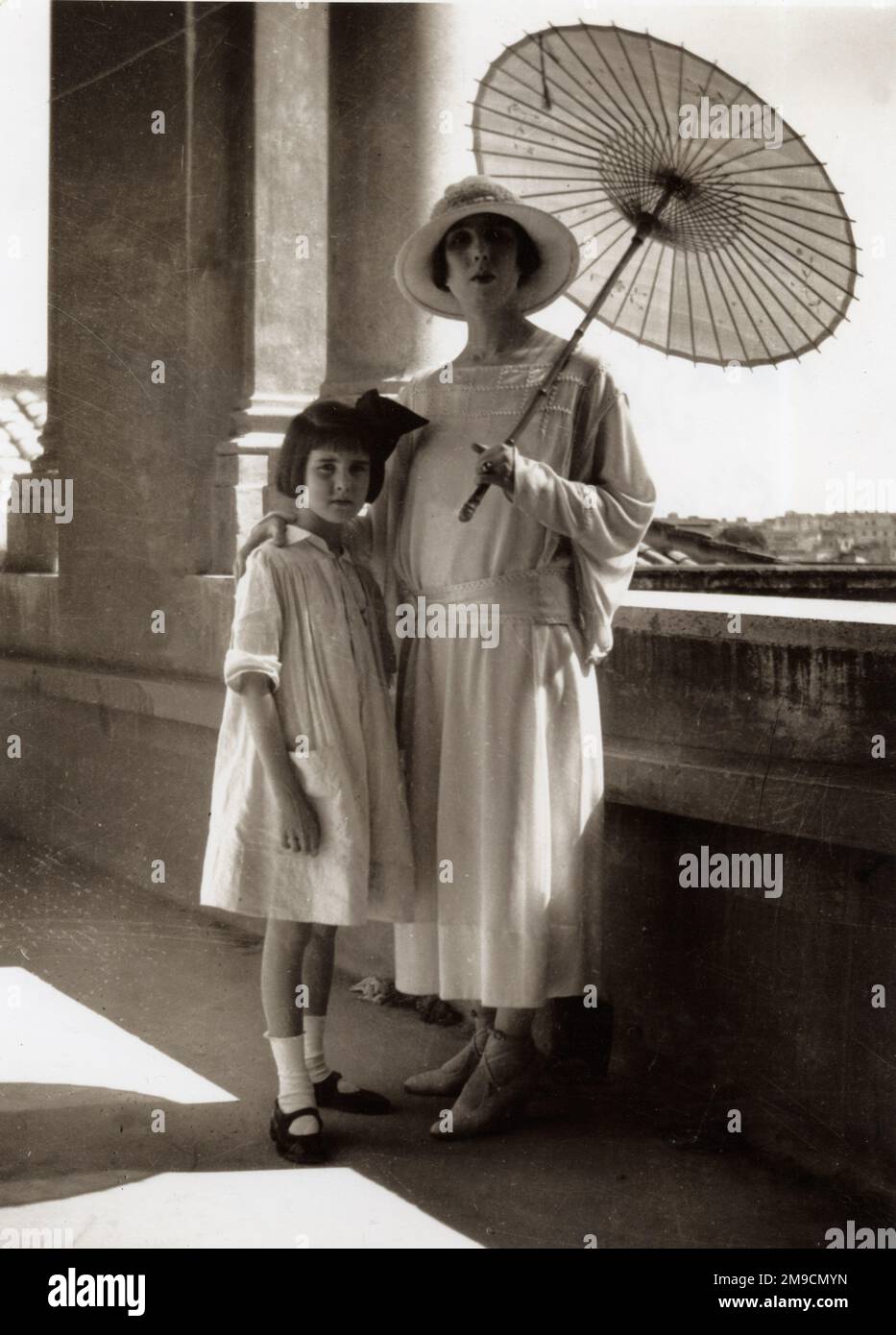 Una donna elegante si posa su un balcone a Roma con la sua figlia. Un parasol cinese di carta protegge la sua carnagione di porcellana senza dubbio dal sole. Foto Stock Una donna elegante si posa su un balcone a Roma con la sua figlia. Un parasol cinese di carta protegge la sua carnagione di porcellana senza dubbio dal sole. Foto Stock