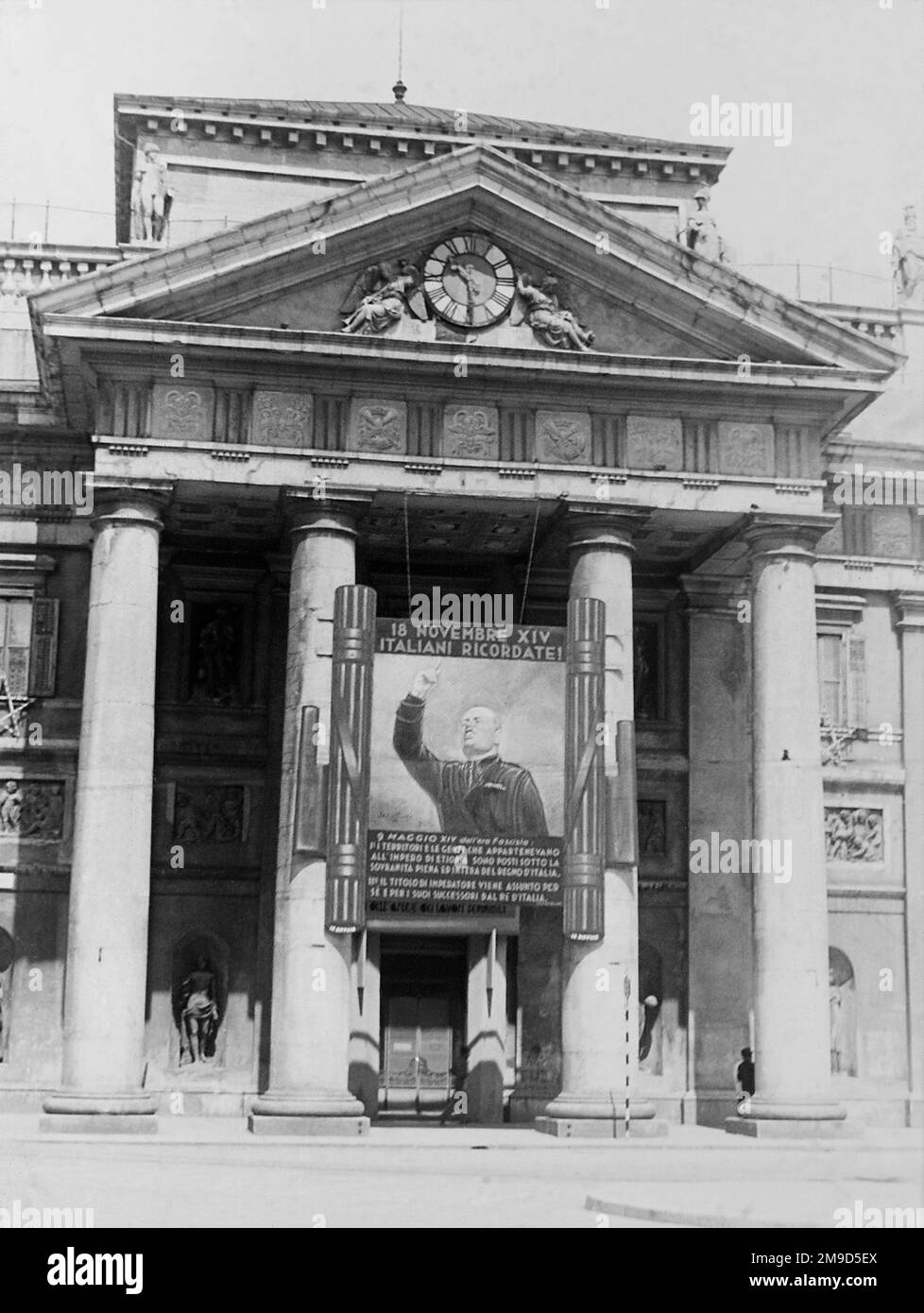 1936 , 27 maggio , TRIESTE , ITALIA : PROPAGANDA fascista italiana , il GIGANTESCO ritratto DIPINTO BENITO MUSSOLINI ingrandimento di fronte alla porta d'ingresso della Borsa MERCI . L'immagine ha celebrato il discorso di Mussolini alla folla che ha proclamato la conquista italiana dell'Etiopia e la proclamazione DELL'IMPERO D'ITALIA il giorno 9 maggio 1936 a Roma . Fotografo sconosciuto . - STORIA - FOTO STORICHE - ROMA - FASCISMO - FASCISTA - FASCISMO - ITALIA - 30'S - '30 - ANNI TRENTA - NOVECENTO - PROPAGANDA - GATTO GUSTO - KITSCH - FASCIO LITTORIO - ARCHITETTURA - ARC Foto Stock
