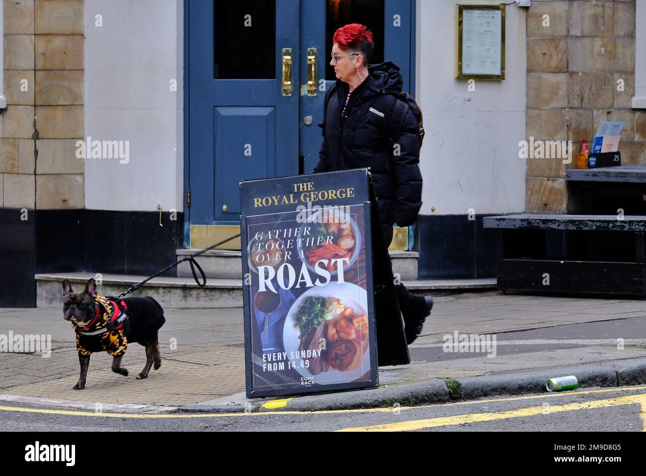 Londra, Regno Unito. Una donna che cammina un cane passa davanti a un pub pubblicità segno per le cene arrosto. Foto Stock