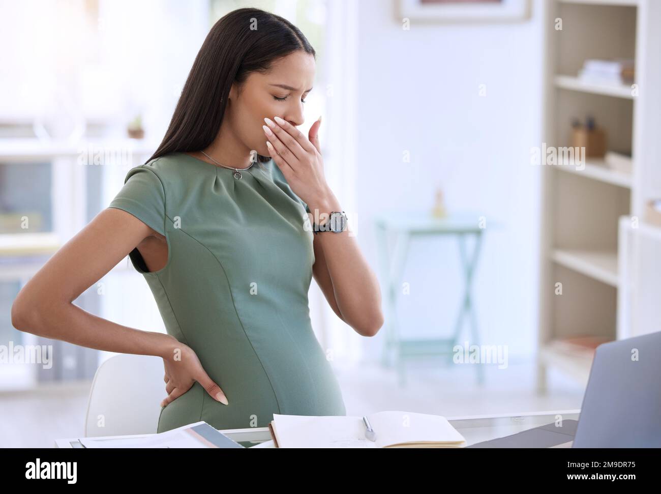 Non mi sento così bene. una giovane donna d'affari incinta seduta da sola nel suo ufficio e coprendo la bocca con la mano. Foto Stock