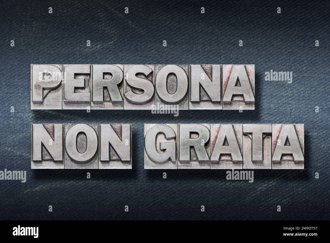 Persona non grata (persona non gradita) frase latina fatta da Letterpress metallico su sfondo di jeans scuro Foto Stock