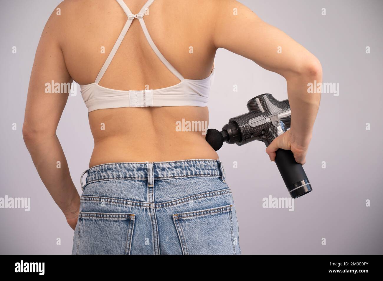 La donna caucasica si fa un massaggio sulla schiena e sui fianchi con una pistola da massaggio. Foto Stock