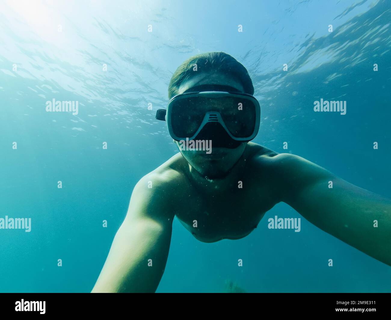 il subacqueo maschile nuota in mare sotto l'acqua con una maschera e lo snorkeling sta prendendo un selfie Foto Stock