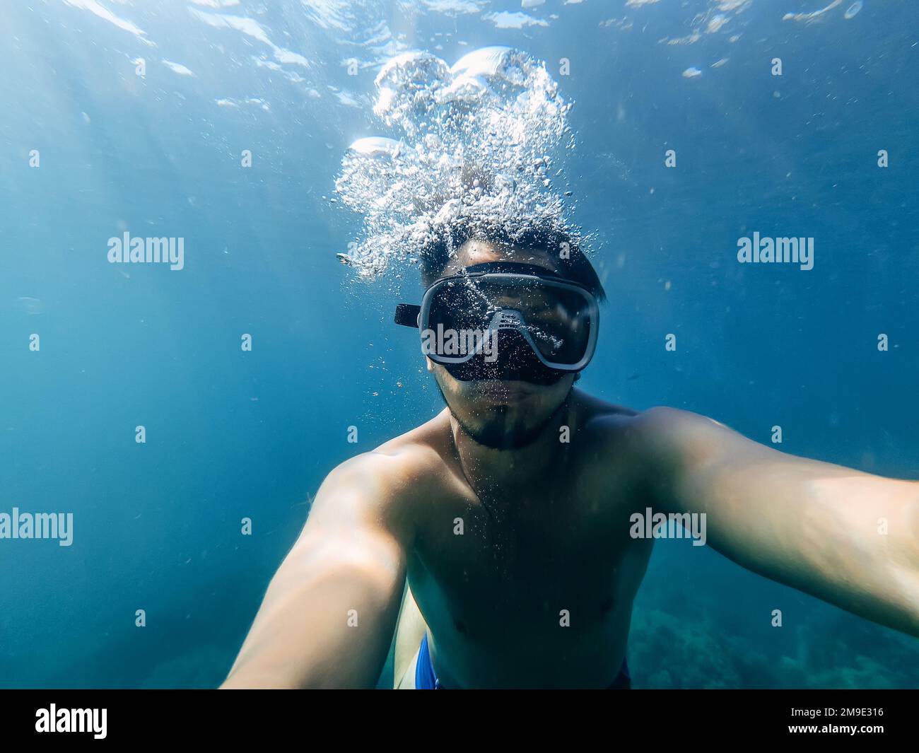 il subacqueo maschile nuota in mare sotto l'acqua con una maschera e lo snorkeling sta prendendo un selfie del tuo volto Foto Stock