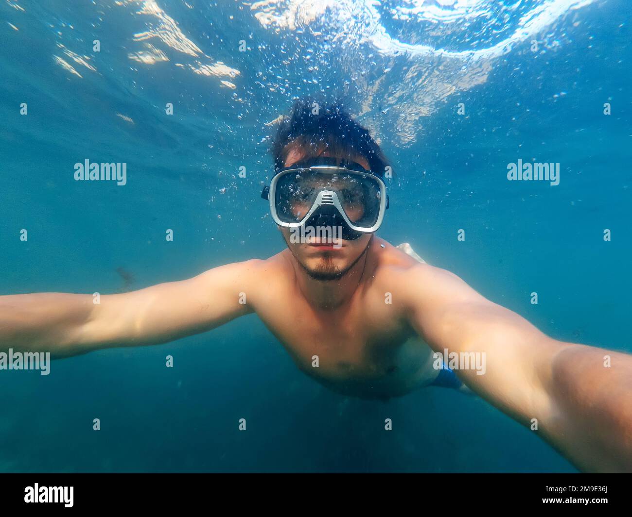il subacqueo maschile nuota in mare sotto l'acqua blu con una maschera e lo snorkeling sta prendendo un selfie Foto Stock