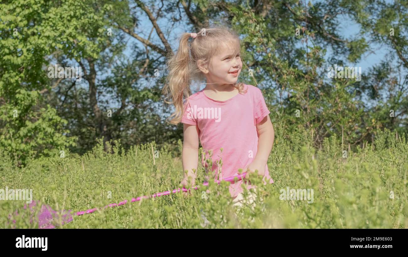La bambina gioca con la rete di farfalle di erba alta nel parco della città. La ragazza piccola carina sta giocando con la rete aerea di insetti nel prato il giorno del sole. Odessa Foto Stock