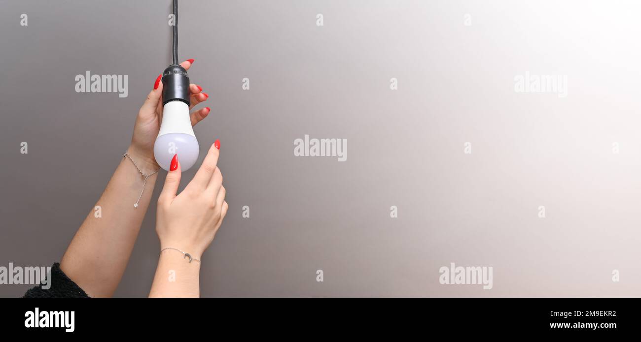 Le mani delle donne con una manicure rossa avvitano una lampada LED elettrica nella cartuccia. primo piano. banner. Foto Stock