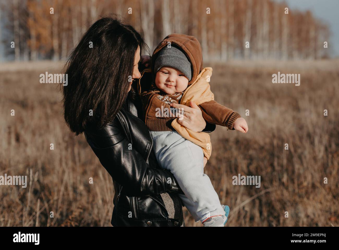 Giovane madre felice e felice con il suo bambino figlio ragazzo nelle sue mani nel campo autunnale. La famiglia felice ha gioia e divertimento Foto Stock