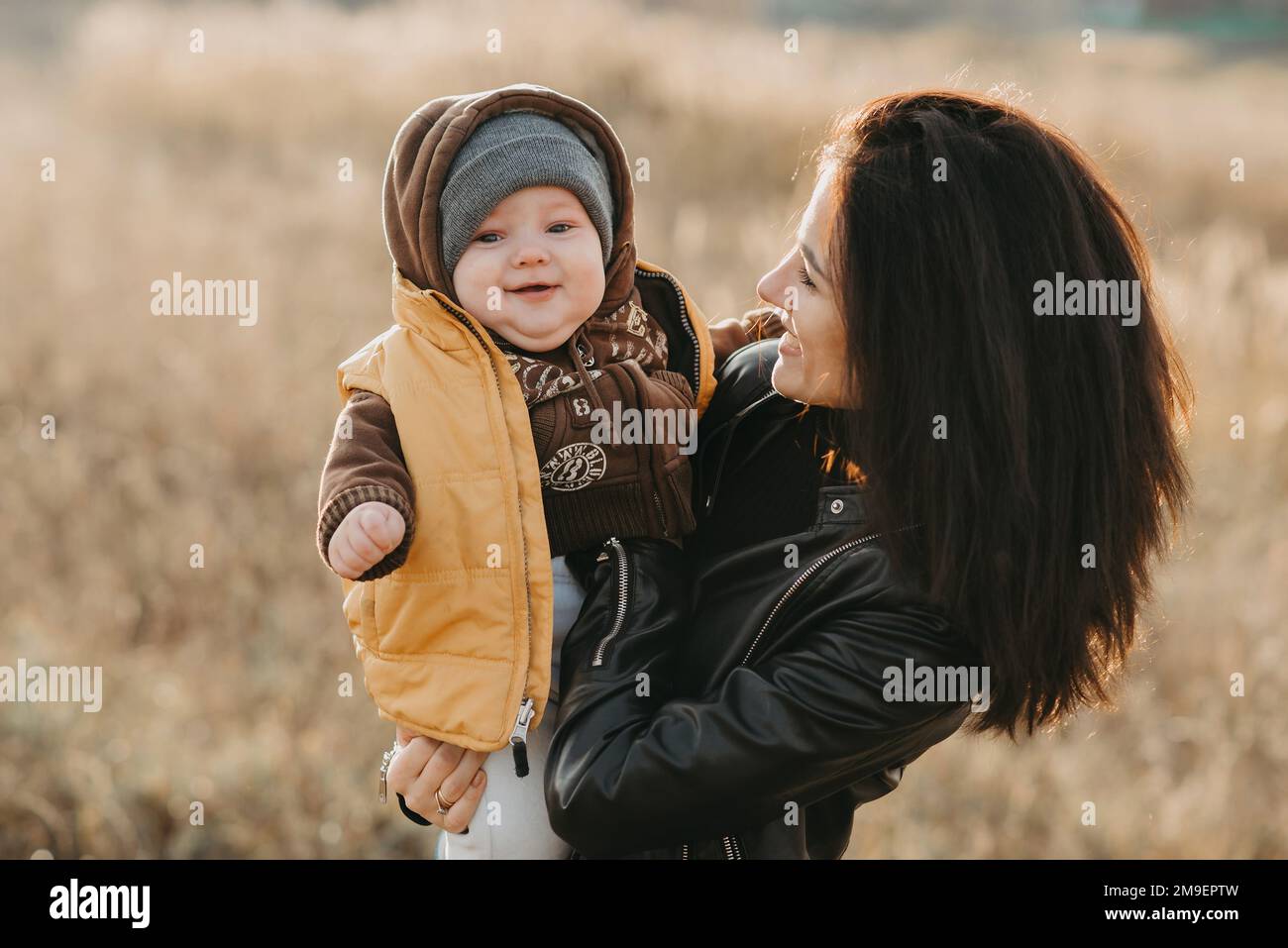 Giovane madre felice e felice con il suo bambino figlio ragazzo nelle sue mani nel campo autunnale. La famiglia felice ha gioia e divertimento Foto Stock
