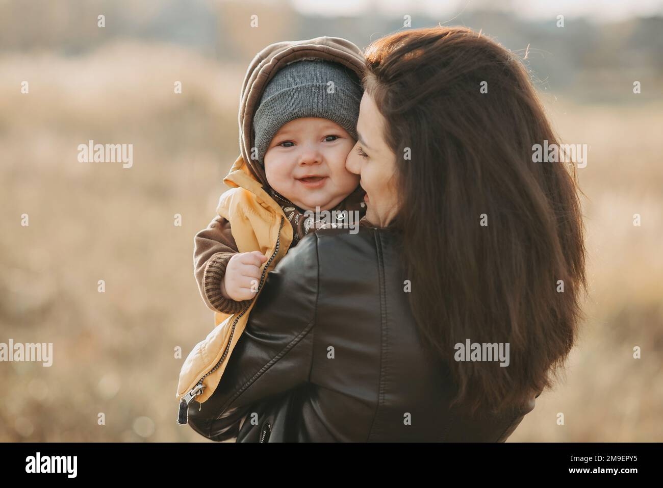 Felice madre e figlio. La giovane ragazza che ride abbraccia il suo bambino tra le braccia in autunno all'aperto Foto Stock