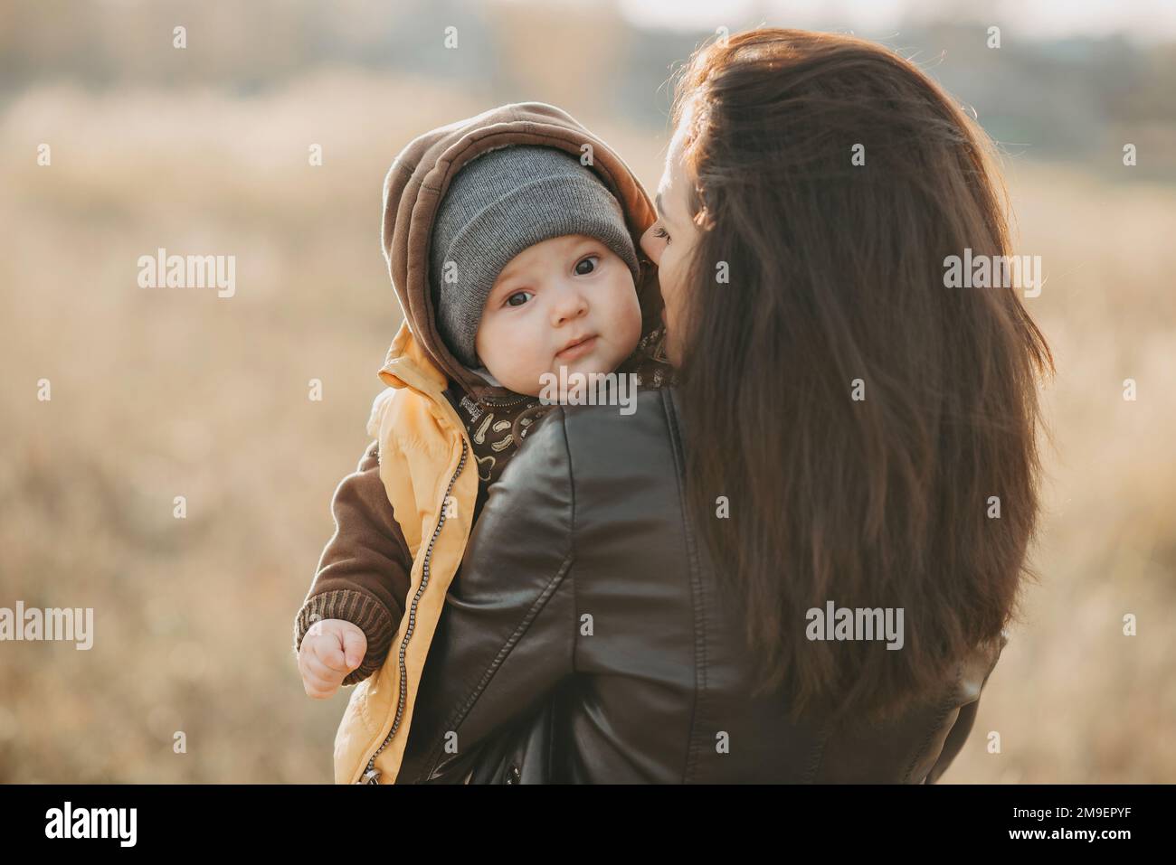 La giovane mamma tiene in braccio il figlio del bambino in autunno sul campo Foto Stock