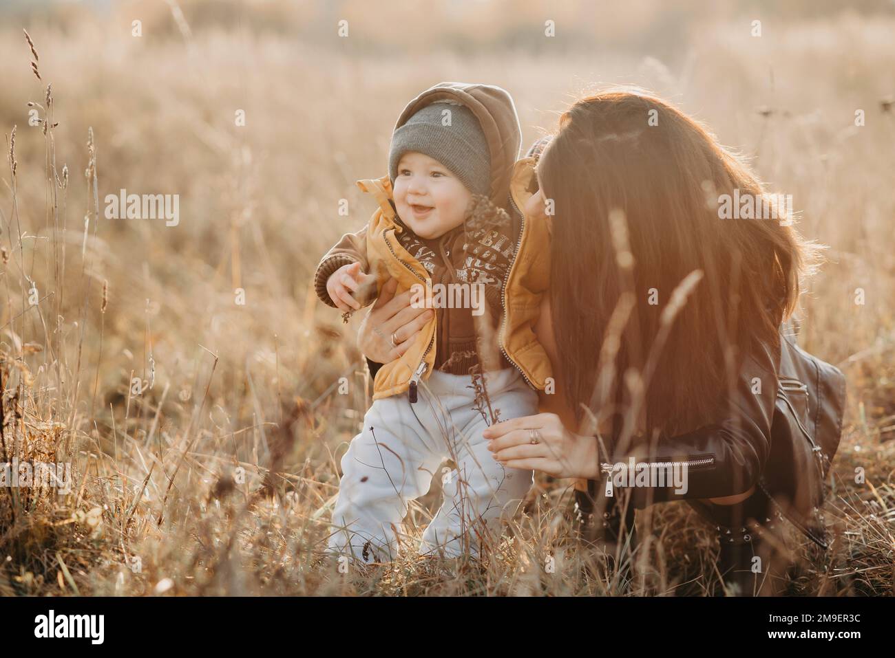 giovane mamma che gioca con il suo bambino figlio in autunno sul campo. Buona passeggiata con la famiglia Foto Stock