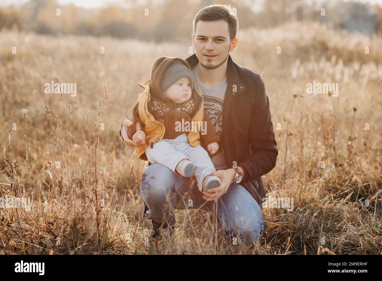 papà giovane con figlio bambino bambino seduto in natura in autunno sul campo. Famiglia sana e felice Foto Stock